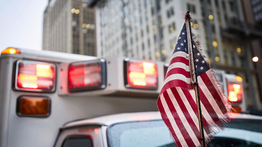 US-Flagge vor Rettungsfahrzeug mit Blaulicht in städtischer Umgebung nach Verkehrsunfall US-Flagge vor Rettungsfahrzeug mit Blaulicht in städtischer Umgebung nach Verkehrsunfall